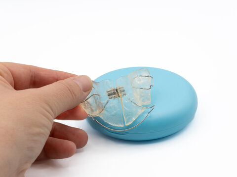 Hand holding clear removable orthodontic dental appliance over a protective case, representing teeth alignment and oral care