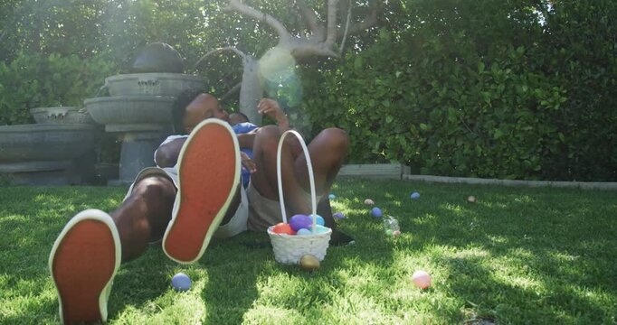 African American father tackling adolescent son in yard, spilling white basket eggs for Easter hunt