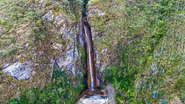 Aerial view of cascading waterfall plunges down the rugged mountain face into a pool surrounded by dense green vegetation, Ollachea, Puno, Peru.