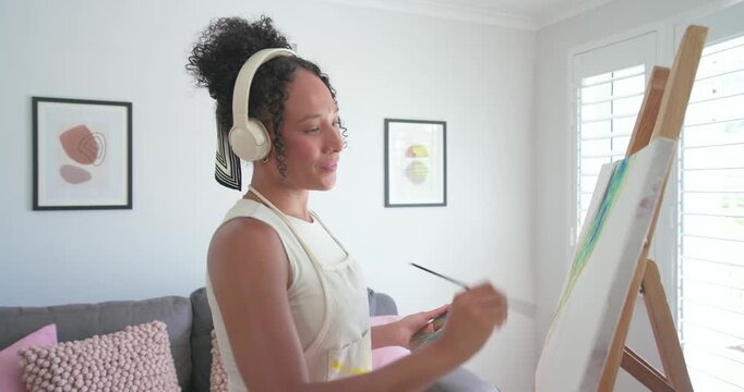 African-American woman in apron painting at easel at home near window, palette, brush refining art