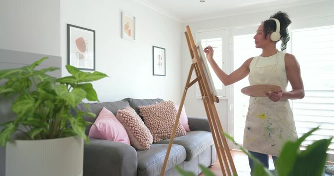 African American woman painting at easel with palette, refining in living room sunlight, copy space