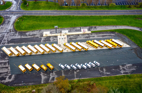 Aerial view of school buses lined up in a parking lot next to a road, a symphony of yellow against the muted asphalt, Hopewell Township, New Jersey, United States.