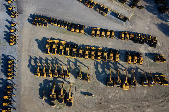 Aerial view of rows of heavy machinery casting long shadows on the gravel lot, a symphony of yellow and gray in Hopewell Township, New Jersey, United States.
