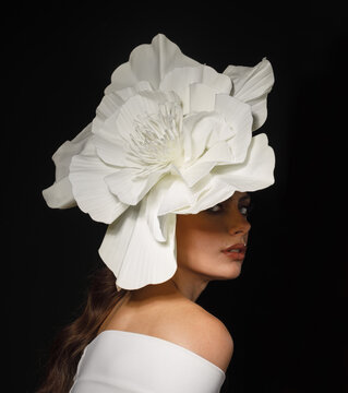 Portrait of woman wearing oversized white flower headpiece on black background. High fashion, creative styling and dramatic beauty concept.
