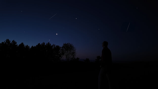 Man looking at night skies, observing Moon, stars, planets and other celestial objects from a dark countryside location.