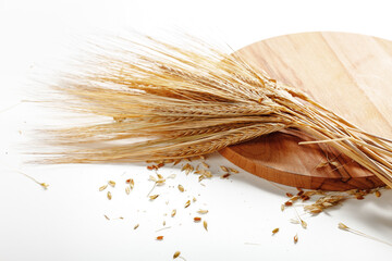 Wheat stalks laid on a wooden board with scattered grains on a white background © fotofabrika