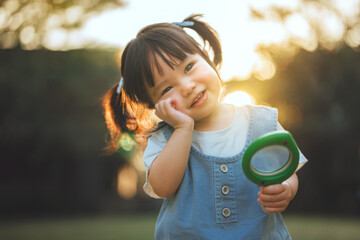 Happy little Asian girl holding toy magnifying glass outdoors, cheerful child exploring nature in the garden, concept of curiosity, STEM education, early childhood discovery, and learning through play