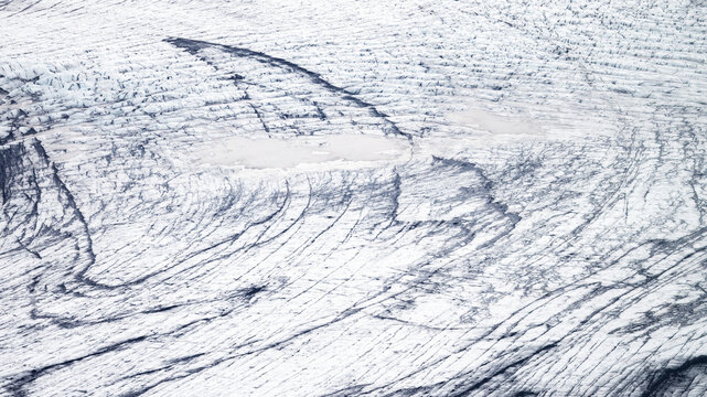 Aerial view of the stark, white expanse of glacial ice, etched with dark, winding crevasses creating a mesmerizing pattern on the frozen landscape, Iceland.