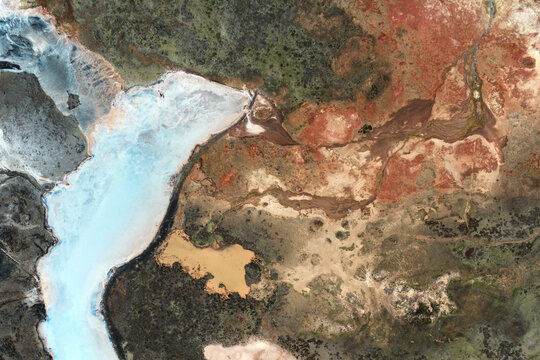 Aerial view of swirling turquoise waters meet the red and brown earth, creating a stunning natural contrast, Iceland.