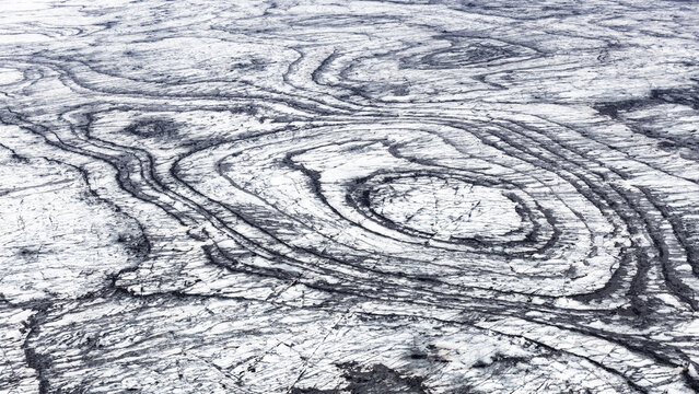 Aerial view of the striking, swirled patterns etched into the glacial ice, a monochrome masterpiece of nature's artistry, Iceland.