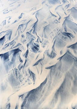Aerial view of glacial rivers weave intricate patterns across the sandy landscape, a symphony of contrasting blues and whites creating an abstract masterpiece, Reykjavik, Iceland.