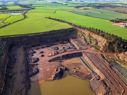 Aerial view of an industrial quarry contrasting sharply with the verdant fields nearby, a testament to human impact on the landscape, Haddington, Scotland, United Kingdom.