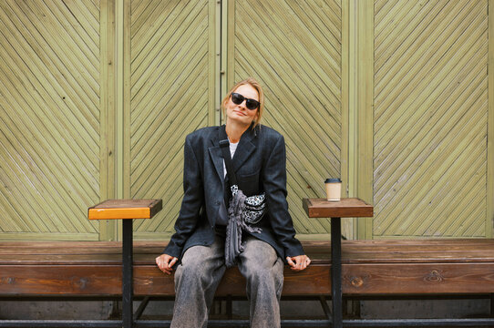 Fashionable Person Sits on Bench Enjoying Coffee in Urban Setting