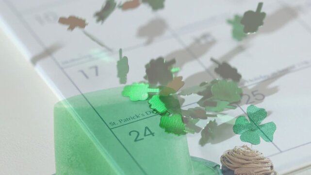 Shamrock confetti appearing above calendar, falling and swirling over hat, cupcake, marking 24-25