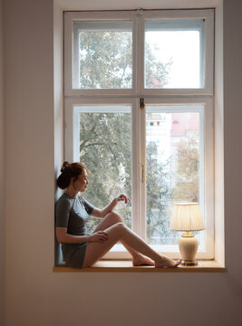 Cozy portrait woman sit on window beside lamp looking outside