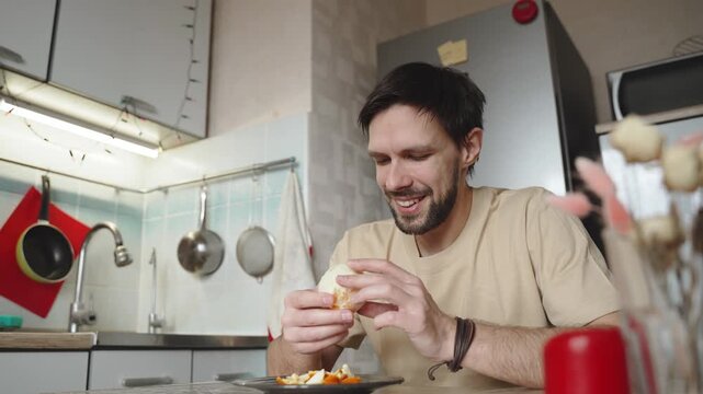 Man is smelling and enjoying aroma of freshly peeled orange in home kitchen. Slender brunette is preparing to consume natural vitamins and fruits during period of vitamin deficiency.