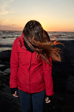 Woman in Red Jacket Standing on Rocky Shore at Sunset