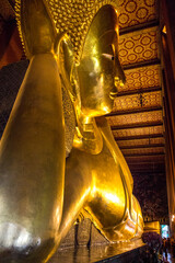 Obraz premium Close up of the colossal Reclining Buddha statue at Wat Pho in Bangkok, Thailand. The entire statue is covered in brilliant, reflective gold leaf that glows under the temple's warm lighting.