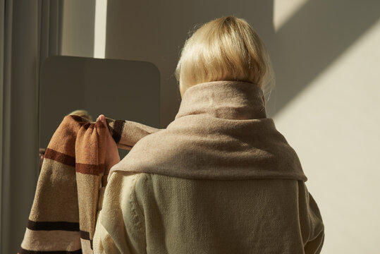 Woman adjusting a cozy scarf in soft sunlight near a large mirror