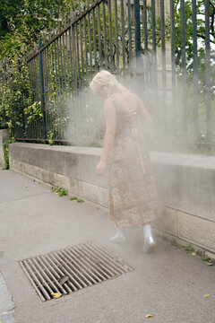 Woman walking in the sidewalk with smoke coming from the underground