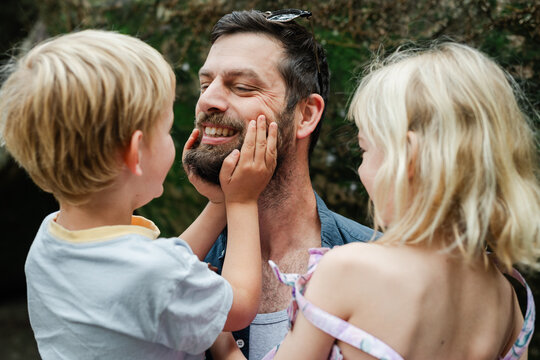 Small children loving on their dad by playing with his face