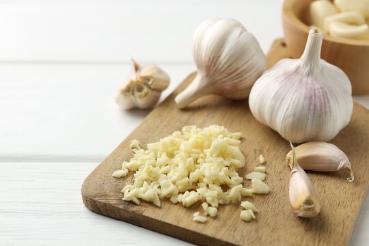 Chopped garlic and bulbs on white wooden table, closeup. Space for text