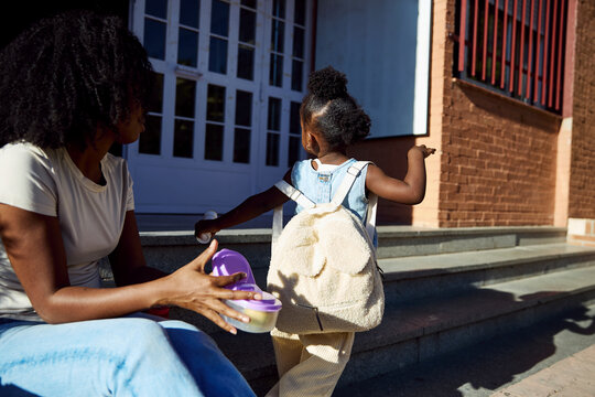 Mother giving lunchbox to daughter before school