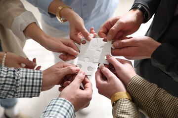 Team building. Group of businesspeople holding puzzle pieces together on blurred light background, closeup