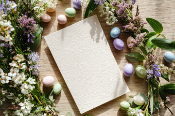 A beautiful arrangement featuring a blank card surrounded by vibrant flowers and pastel colored Easter eggs, perfect for festive greetings.