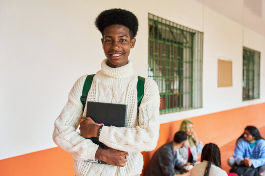 Smiling african american student holding laptop in hallway