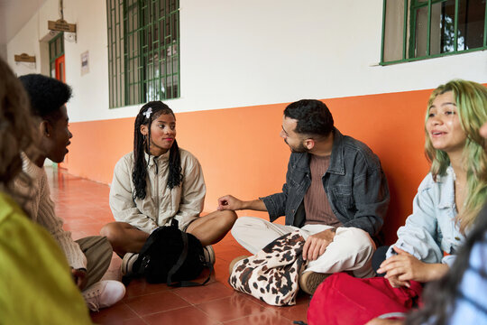 Diverse students sitting on floor discussing in hallway
