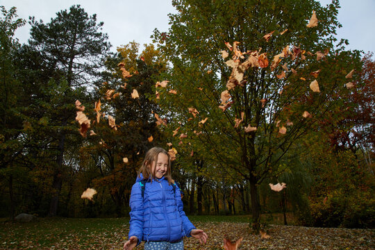 A young girl throwing brown leaves at a park 