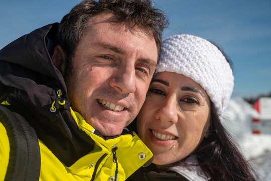 Very narrow close-up of a man and a woman on a snowy mountain. The two are about forty years old and of Caucasian origin. The man is wearing a yellow jacket, the woman has a white band on her forehead