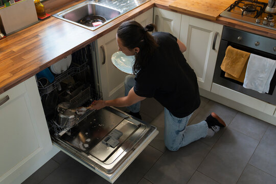 Young Man Organizes Dishes in Dishwasher During Household Chores