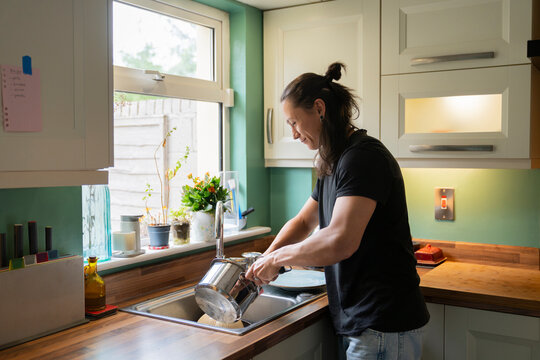 Young Man Washes Dishes in Bright Kitchen During Daytime