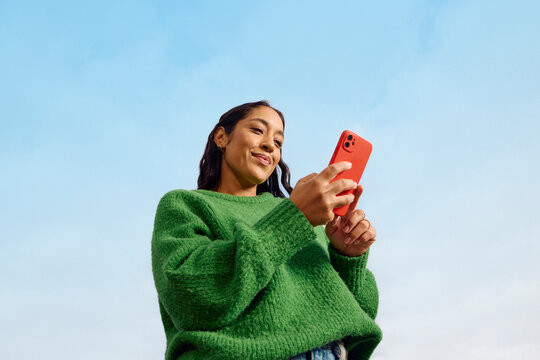 Pleased woman uses her mobile phone outdoors