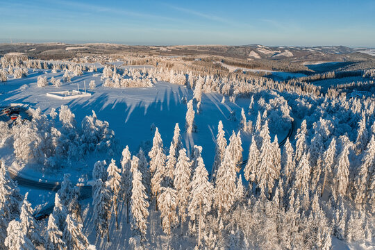 Aerial view of a snow-covered forest casting stark shadows under a clear sky, a winter wonderland in Germany., Winterberg, North Rhine-Westphalia, Germany.