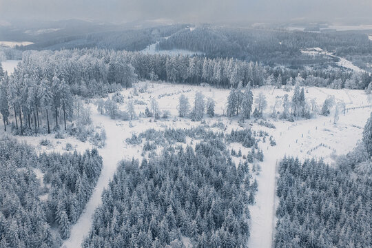 Aerial view of snow-dusted trees and frosted fields create a serene winter wonderland under a soft, overcast sky, Winterberg, North Rhine-Westphalia, Germany.