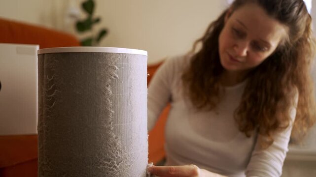 Diligent woman meticulously removing a large clump of dust and dirt from a clogged air purifier filter during routine home maintenance, ensuring fresh and clean air in her apartment