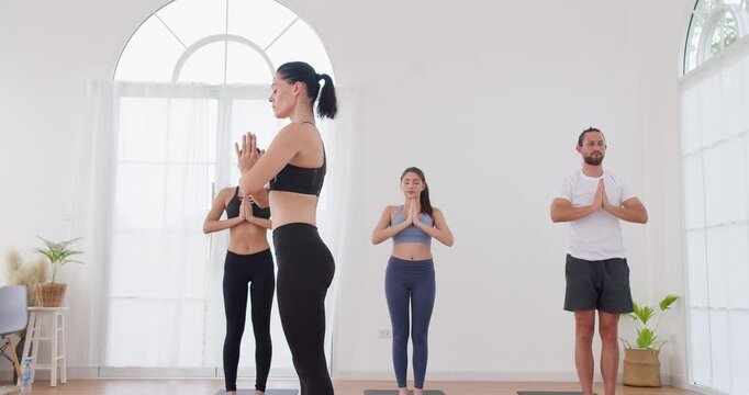 Professional yoga instructor is leading a group meditation practice in a bright minimalist studio, focusing on holistic wellbeing, mindfulness, and physical health.