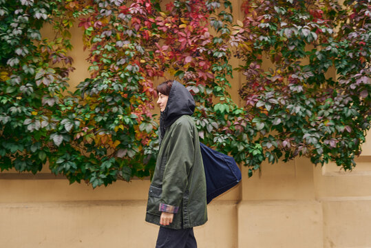 A woman strolls through a wall surrounded by vibrant vines.