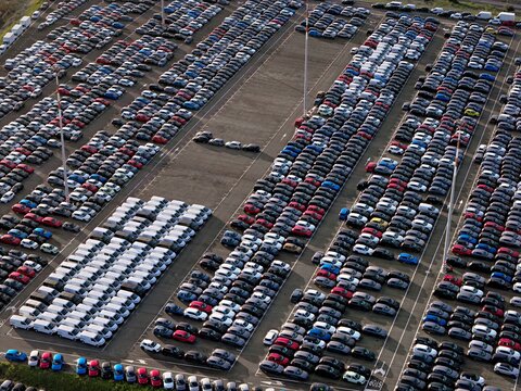 Aerial view of row upon row of tightly packed cars in an expansive lot create a mesmerizing geometric pattern under the sky, Civitavecchia, Lazio, Italy.
