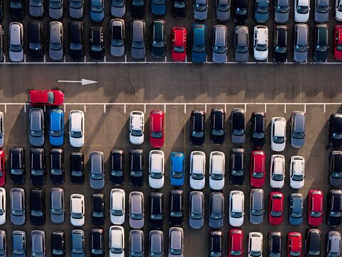 Aerial view of a sea of cars, neatly aligned in rows, their colors popping against the stark asphalt, divided by white lines, Civitavecchia, Lazio, Italy.