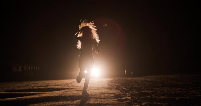 Silhouette of girl running towards car headlights at night in an empty landscape