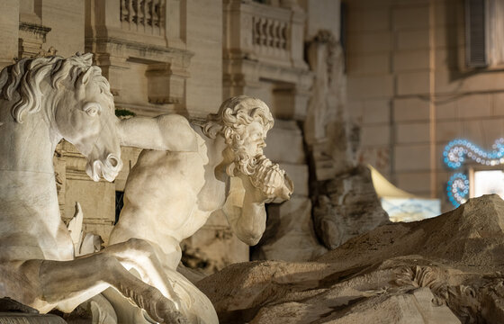 Trevi Fountain marble triton blowing a conch shell while guiding a rearing seahorse, ornate Baroque sculpture illuminated at night in Rome, Italy, close up detail