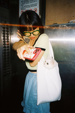 Young woman holding her cellphone while her cat is in her tote bag.