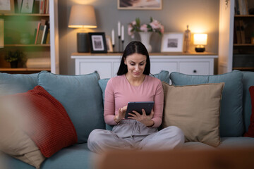 Obraz premium Woman relaxing at home using digital tablet on sofa