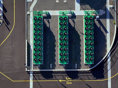 Aerial view of the symmetrical array of green industrial cooling units casting stark shadows on the dark asphalt, Civitavecchia, Lazio, Italy.
