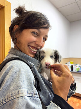 Smiling Woman Feeding Blue Merle Border Collie Puppy Indoors