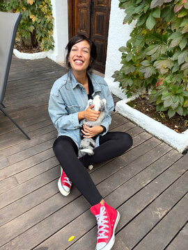 Smiling Woman Sitting With Puppy On Wooden Deck